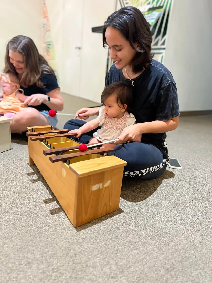 Two grown-ups with babies on their laps play a wooden xylophone
